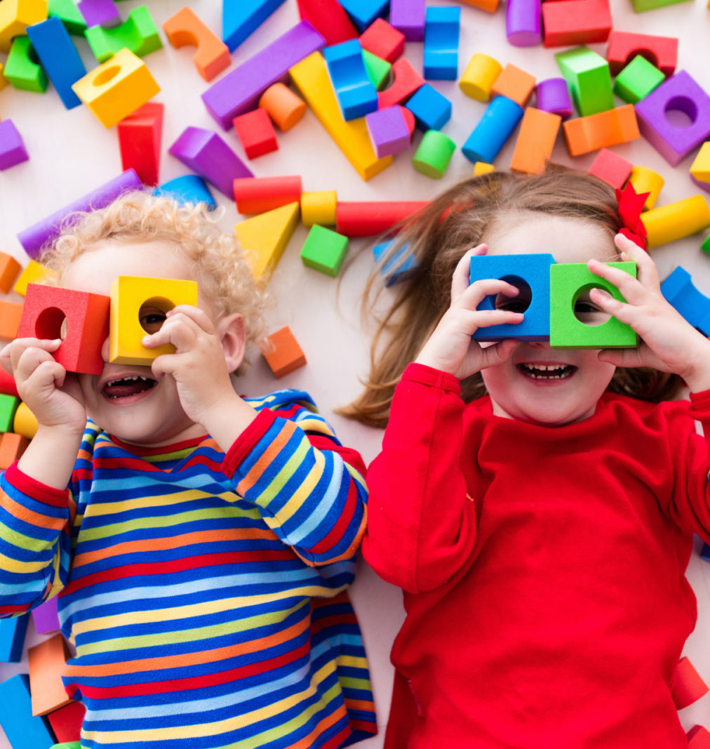 Happy preschool age children play with colorful plastic toy blocks. Creative kindergarten kids build a block tower. Educational toys for toddler or baby. Top view from above.