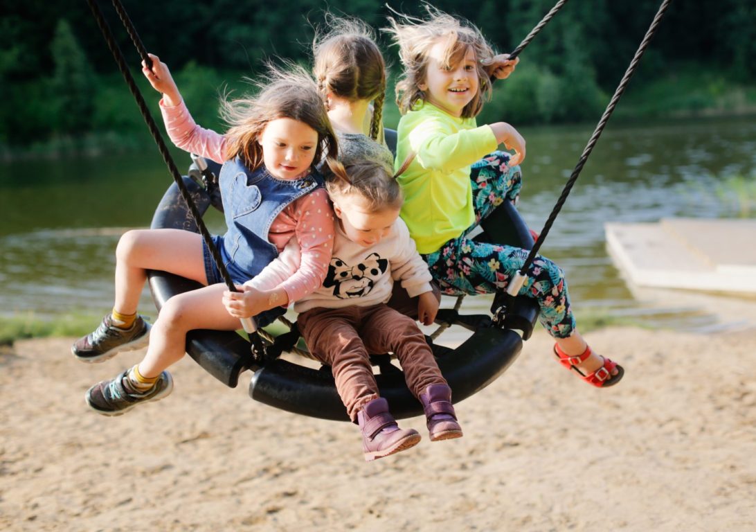 four children swinging on wicker swing on playground in park by lake, Sand and children's summer vacation with friends
